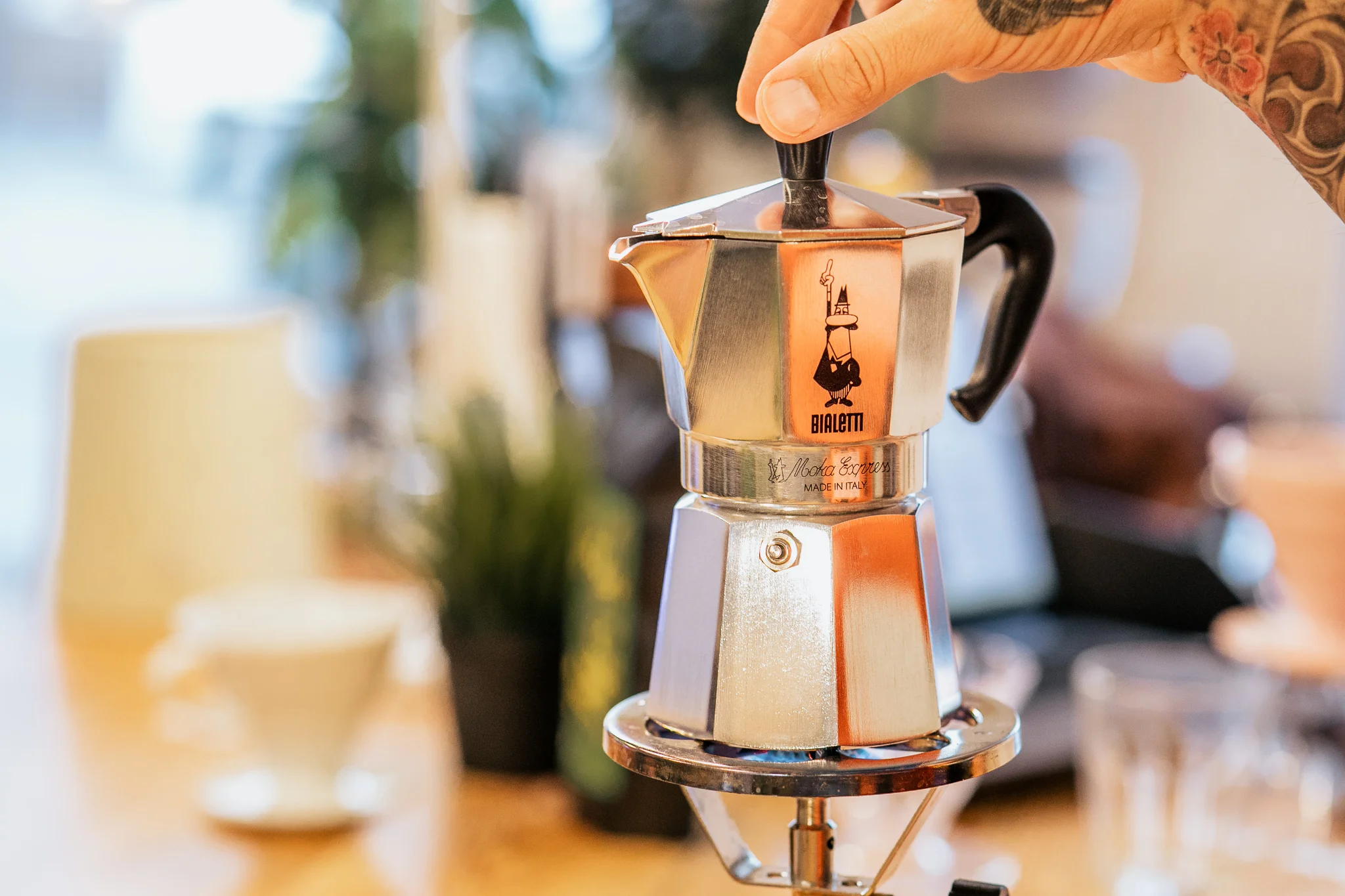 Tradycyjna, srebrna kawiarka aluminiowa Bialetti Moka Express trzymana za uchwyt nad palnikiem w kawiarni lub kuchni.